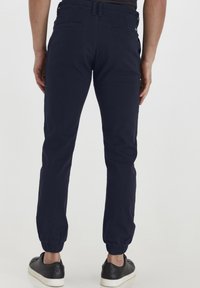 Marinblå joggebukser laget av bomull med elastisk midjebånd og mansjetter, med to baklommer og en slim fit-design.