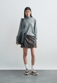 Šedý dlouhý rukáv turtleneck, hnědá kožená mini sukně s švy. Černá kabelka, bílé ponožky a tenisky v béžové/černé barvě.