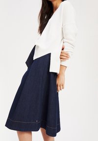 Pull en tricot blanc avec des poignets côtel és, associé à une jupe A en denim foncé présentant un ourlet visible et des détails de couture.