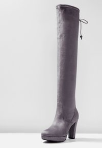 Bota de ante gris, por encima de la rodilla, con un alto tacón bloque, punta redondeada y detalle de cordón ajustable en la parte superior. Diseño sin costuras.