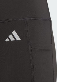 Leggings atléticos negros de tejido elástico. Incluyen un bolsillo lateral, costuras planas y un logo de marca blanco cerca de la cintura.