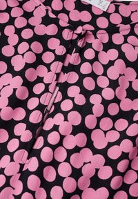Sort stof med pink cirkulære mønstre. Har en knaplukning og et lille bånd ved halsudskæringen. Blød tekstur med et let draperet design.