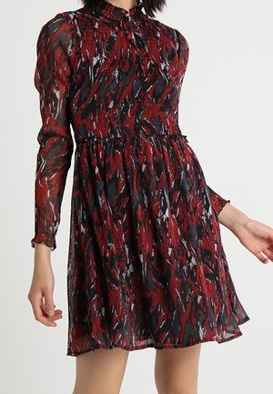 Robe rouge et noire à manches longues, longueur genoux, avec motif abstrait, col montant à volants et taille froncée sur une personne debout.