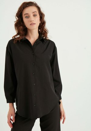 Zwarte button-up shirt met een kraag, lange mouwen en een gebogen zoom, gemaakt van een gladde stof. Voorzien van zwarte knopen aan de voorkant.