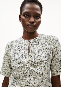 Kurzärmlige Bluse aus hellgrünem Stoff mit einem gedruckten Muster aus marineblauen Formen, mit Rundhalsausschnitt und vorderer Raffung.