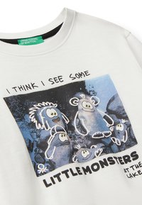 Weißer Baumwoll-Sweatshirt mit einem grafischen Druck von cartoonartigen Kreaturen und dem Text "ICH DENKE, ICH SEHE EINIGE KLEINE MONSTER AM SEE."