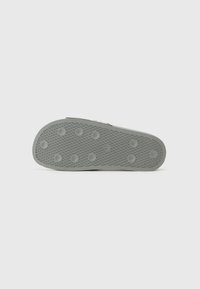 Shoe sole in light gray rubber with circular grip patterns and textured surfaces. Features a rounded shape with raised circular accents.