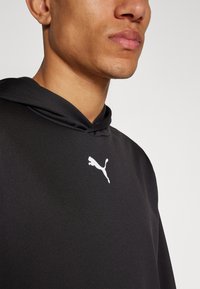 Crna dukserica od glatkog materijala s bijelim Puma logotipom. Dizajn uključuje kapuljaču i ležeran kroj.