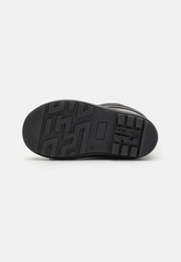 Suela de zapatilla negra con superficie de goma texturizada, que presenta un patrón de banda de rodadura geométrico y un corte rectangular central para mayor flexibilidad.