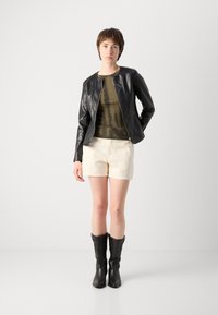 Black faux leather jacket with a fitted design, olive green tie-dye top, cream shorts, and knee-high black cowboy boots.
