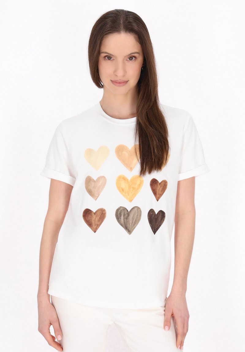 Hvid T-shirt med trykt design af ni hjerter i forskellige nuancer af beige og brun, præsenteret i et gittermønster. Korte ærmer.