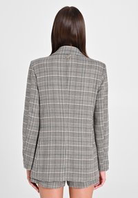 Blazer a quadri in grigio e nero, con una silhouette sartoriale, revers a punta e un dettaglio del logo metallico sul retro. Tessuto testurizzato.