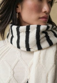 Écharpe tricotée avec des rayures noires et blanches alternées, présentant un tissage épais et texturé. L'écharpe est enroulée autour du cou.