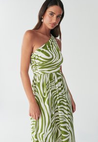 Grøn og hvid asymmetrisk kjole med zebrastribet mønster, rynket overdel og flydende nederdel. Letvægtsstof med blød tekstur.