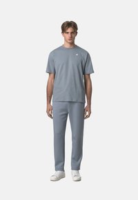 Maglietta in cotone grigio chiaro con colletto rotondo e maniche corte, abbinata a pantaloni grigio chiaro coordinati. Sneakers bianche completano l'outfit.