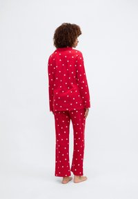 Κόκκινο σετ πιτζάμας με λευκά σχέδια καρδιάς. Μάκρος μανίκι και παντελόνια κατευθείαν σε μαλακό ύφασμα. Μινιμαλιστικός σχεδιασμός, χωρίς ορατό hardware ή αξεσουάρ.