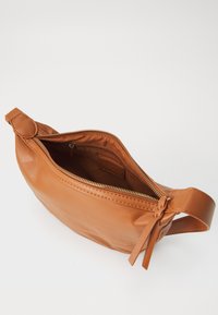 Bolsita de cuero color marrón claro con cierre de cremallera, forma curva y detalle de nudo lateral. Textura suave, con un bolsillo interno visible.