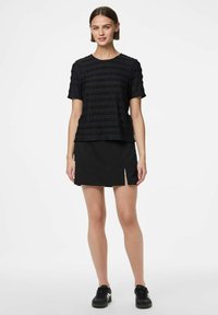 Sort tekstureret t-shirt med korte ærmer og vandrette striber, parret med en sort miniskirt med en frontslids, kompletteret med sorte sneakers.