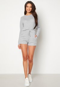 Completino in maglia grigia con maniche lunghe, vita regolabile con cordino e pantaloni corti. Presenta una texture a costine. Abbinato a sneakers bianche.