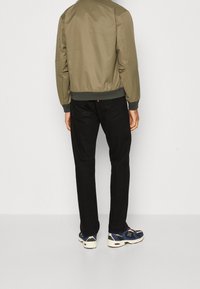 Oliivinvihreä pommitakki, jossa on resorit hihansuissa ja helmassa, yhdistettynä mustiin housuihin ja sinisiin lenkkareihin, joissa valkoiset pohjat ja yksityiskohdat.