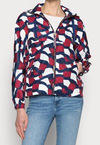 Rood, wit en blauw gestreepte windbreaker met een rits, een trekkoordkap en elastische manchetten. Gemaakt van lichte, glanzende stof.