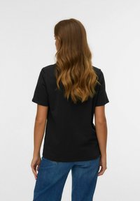 T-shirt nera in cotone con maniche corte, vestibilità comoda e colletto tondo. Abbinato a jeans in denim blu. Vista posteriore che mostra capelli castani mossi.