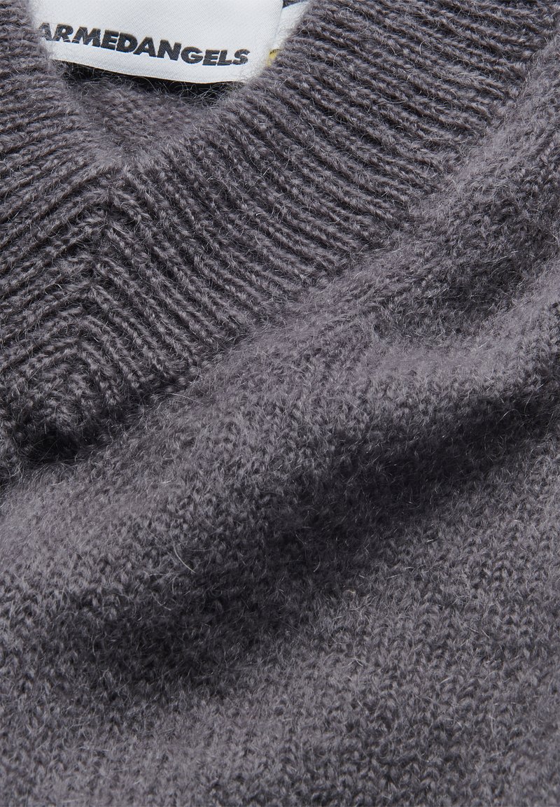 Grijze gebreide trui met een gestructureerde, zachte stof, een V-halsontwerp en een zichtbaar logo-label, dat een mix van gladde en fuzzy garens toont.