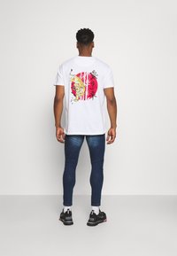 White cotton t-shirt featuring a colorful tiger design on the back, paired with dark blue fitted jeans and black sneakers.