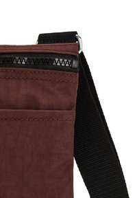 Mörkröd tygaxelväska med svart rem, med en dragkedjeficka och texturerat material. Kompakt design med minimal dekoration.