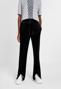 Zwarte corduroy broek met een relaxte pasvorm, voorzien van een trekkoord in de taille, zijsplitten bij de manchetten en gecombineerd met een grijze geometrische graphic t-shirt.