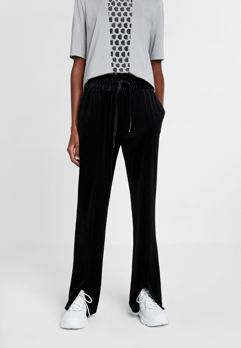 Zwarte corduroy broek met een relaxte pasvorm, voorzien van een trekkoord in de taille, zijsplitten bij de manchetten en gecombineerd met een grijze geometrische graphic t-shirt.