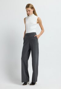 Top de punto sin mangas blanco ajustado combinado con pantalones de pierna ancha grises, ajustados, con bolsillos frontales y un sutil estampado de rayas verticales.