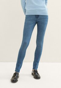 Jeans ajustados de mezclilla azul medio, con una textura suave y un desgaste mínimo. Combinados con zapatos negros de cordones.