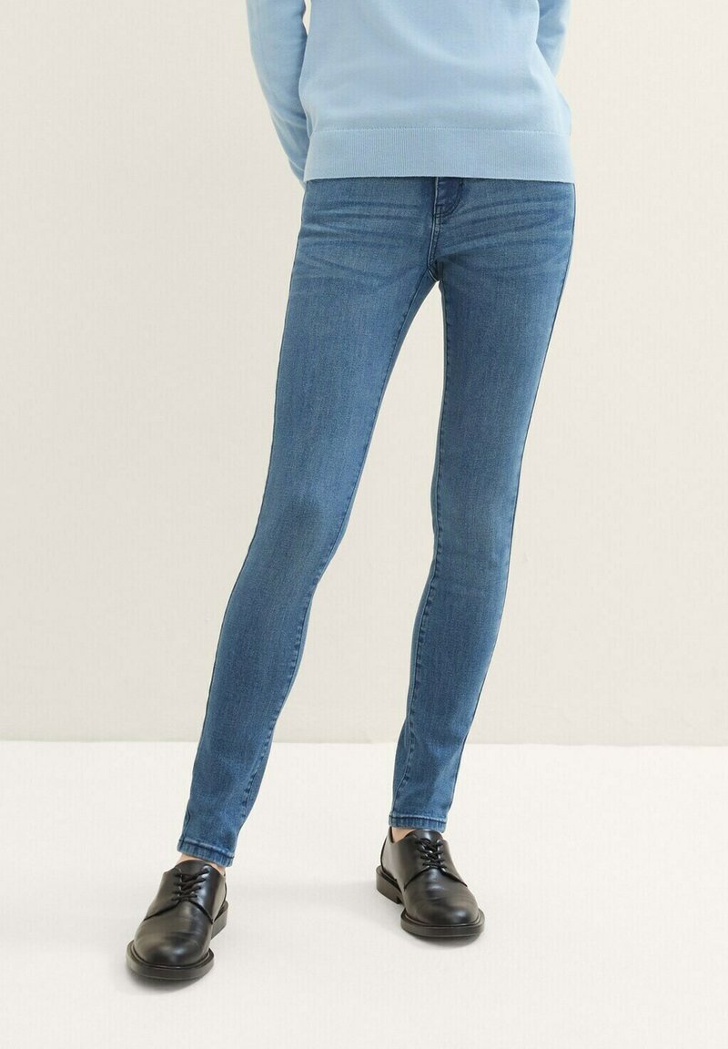 Jeans ajustados de mezclilla azul medio, con una textura suave y un desgaste mínimo. Combinados con zapatos negros de cordones.
