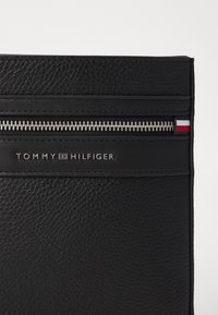 Black leather wallet featuring a zippered compartment, textured surface, and an embossed logo. Includes a color accent in red, white, and blue.