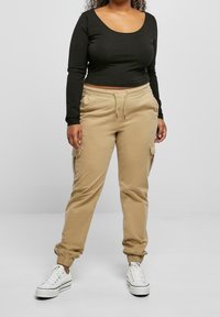 Black long-sleeve top with a scoop neckline paired with beige cargo pants featuring side pockets and elastic cuffs, worn with white sneakers.