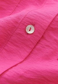 Dettaglio di tessuto rosa con una superficie liscia e testurizzata e un bottone circolare di colore chiaro cucito lungo il bordo.