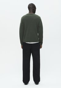 Green knitted sweater with a round neck, paired with loose-fitting black pants. Smooth texture; plain design without patterns or accents.