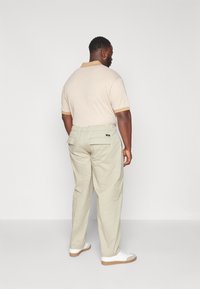 Polo a righe in crema e marrone, abbinato a pantaloni beige chiaro con tasche posteriori e vita elasticizzata, completato da sneakers bianche.