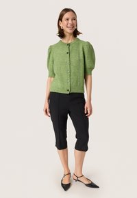 Grøn strikket cardigan med korte puffærmer og rund halsudskæring, med dekorative knapper og ribbet kant. Parret med sorte cropped bukser.