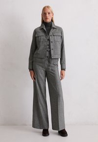 Giacca in misto lana grigia con quattro tasche frontali, abbinata a pantaloni a gamba larga coordinati. Presenta un colletto e chiusure con bottoni.