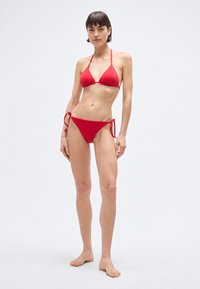 Set bikini rosso con top a triangolo e slip con laccetti ai lati. Realizzato in tessuto liscio, leggero e dal design minimalista.