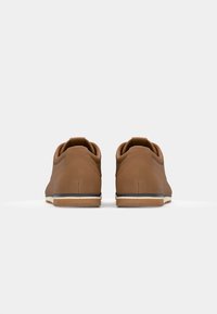Zapatos de cuero sintético marrón con un diseño redondeado, que cuentan con una suela plana, una textura suave y una lengüeta trasera para facilitar su puesta.