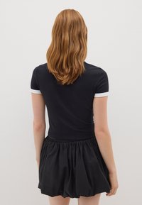 Top aderente nero con accenti bianchi ai polsini abbinato a una gonna nera ampia; tessuto liscio con elastico in vita, creando una silhouette rilassata.