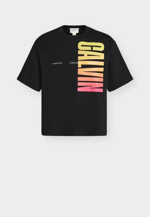 Svart kortermet t-skjorte med "CALVIN" i vertikal gradienttekst fra gul til rosa og liten hvit tekst "Calvin Klein" og steder.