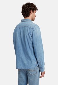 Lichtblauwe denim overhemd met lange mouwen, knoopmanchetten en een klassieke kraag. De stof heeft een zachte textuur en een ontspannen pasvormontwerp.