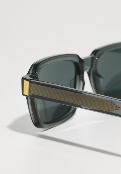 Sunglasses with rectangular dark lenses, gray transparent frame, and textured gold accents on the temples. Sleek, modern design.