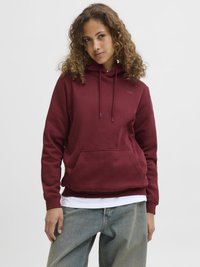 Burgunderfarget hettegenser med kengurulomme, justerbar snorhette og ribbestrikkede mansjetter, lagd over en hvit skjorte, kombinert med løse jeans.
