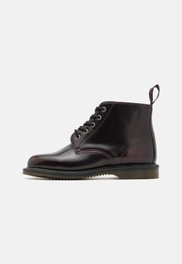 Braune Lederanboot mit runder Spitze, Schnürdesign, metallischen Ösen und einer strukturierten Sohle. Mit einer Schlaufe hinten.