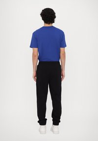 Blå kortærmet t-shirt og sorte joggerbukser med en afslappet pasform og manchetter ved anklene, parret med hvide fodtøj.
